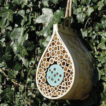 Dewdrop Bee and Bug Hotel hanging outside on a background of Ivy. Featuring a woven wood exterior and the inside of the dewdrop filled with small wooden tubes. Natural rope hanger and rustic apperance. 